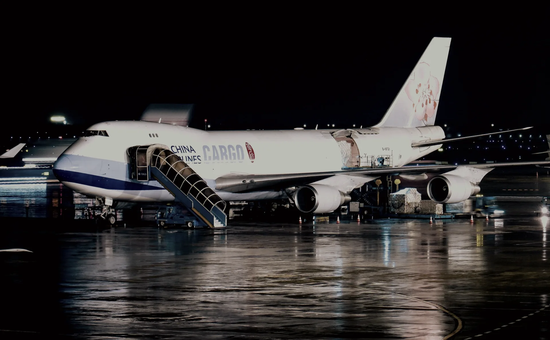 Freighter aircraft being worked on a wet ramp at night, cargo pallets alongside